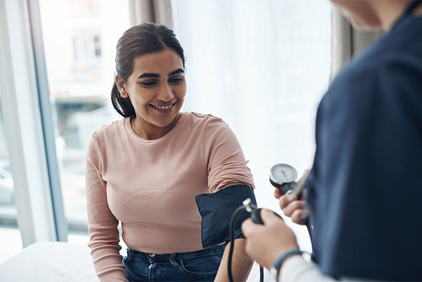 Young Hispanic female volunteer nurse checks a mid adult woman's blood pressure in free medical clinic.